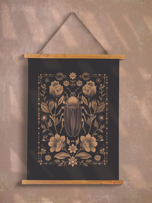 A symmetrical wall tapestry featuring a large scarab beetle in antique bronze tones surrounded by detailed flowers and botanical elements on a black background, mounted on wooden dowels with twine.